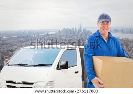 Happy delivery man holding cardboard box against new york