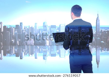 Businessman looking up holding laptop against mirror image of city skyline