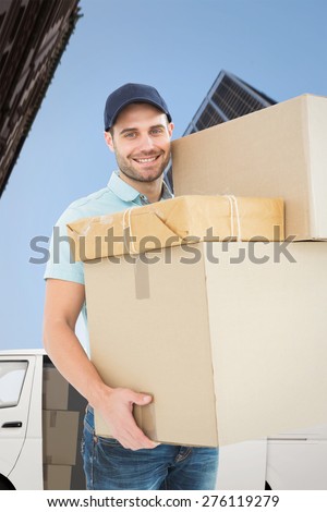 Happy delivery man carrying cardboard boxes against skyscraper