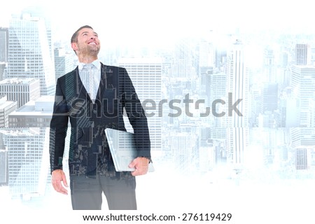 Businessman looking up holding laptop against room with large window looking on city
