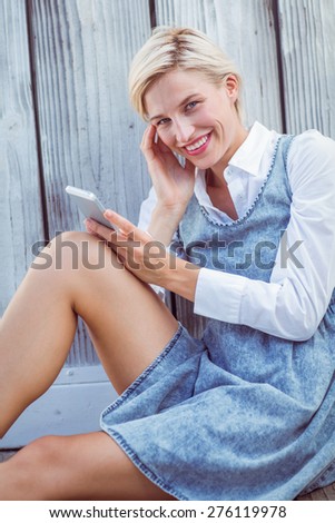 Pretty blonde texting with her mobile phone on wooden background