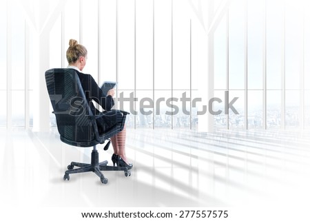 Businesswoman sitting on swivel chair with tablet against room with large window looking on city