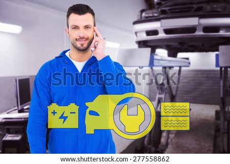 Smiling male mechanic using his mobile phone against auto repair shop