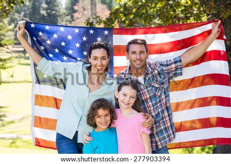 Happy family smiling with an american flag in a park on a sunny day