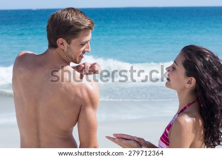 Pretty brunette putting sun tan lotion on her boyfriend at the beach