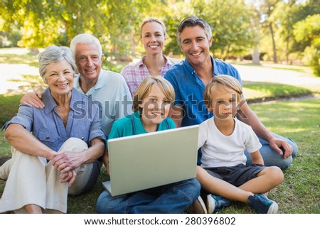 Happy family smiling at camera and using laptop in the park on a sunny day