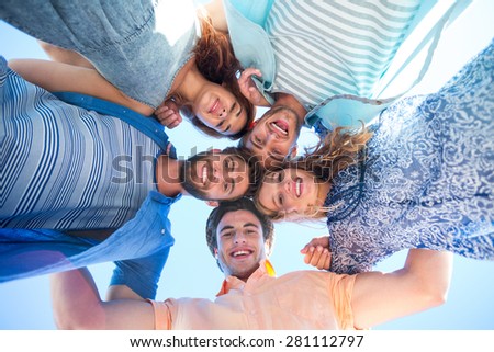 Happy friends standing in circle and looking at camera at the beach