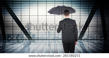 Businessman sheltering under black umbrella against room with large window looking on city