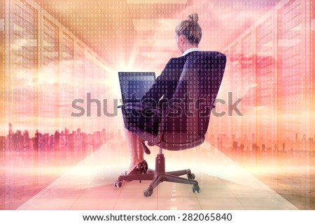 Businesswoman sitting on swivel chair with laptop against server room with towers