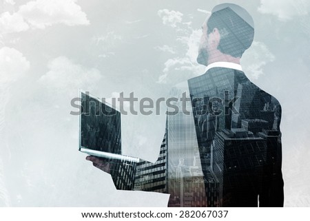 Businessman looking up holding laptop against low angle view of skyscrapers