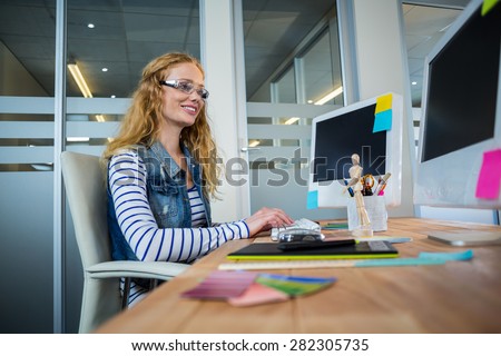 Smiling designer sitting at her desk and typing on keyboard in the office