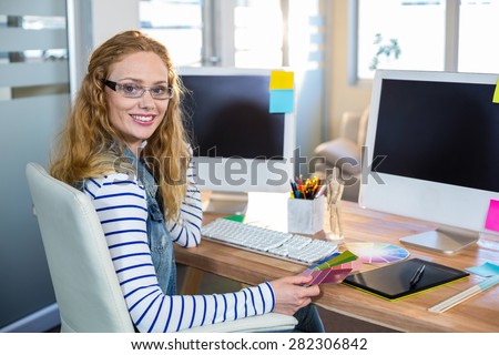 Smiling designer sitting at her desk and looking at colour swatch in the office