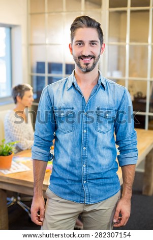 Smiling man looking at camera with his partner behind in the office