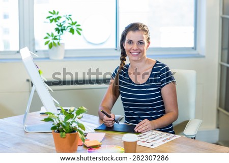 Smiling designer sitting at her desk and working with digitizer in the office