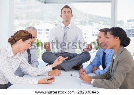 Businessman relaxing on the desk with upset colleagues around in the office