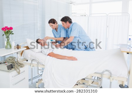 Worried doctors doing heart massage and holding oxygen mask in hospital room