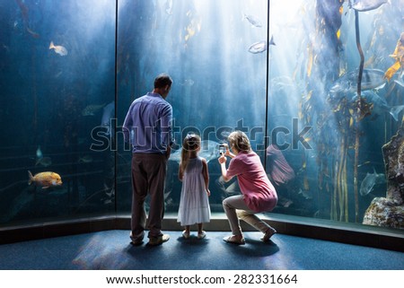 Mother taking photo of fish while daughter and father looking at fish tank at the aquarium