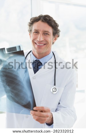 Happy doctor holding X-ray and smiling at camera in medical office