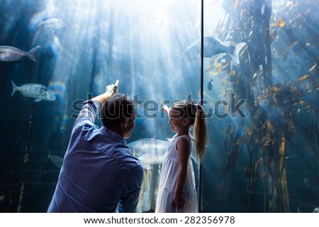 Father and daughter pointing a fish in the tank at the aquarium