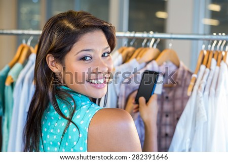 Beautiful brunette scanning bar code with her mobile phone in clothes store