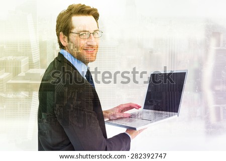 Smiling businessman using a laptop against room with large window looking on city