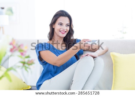 Smiling beautiful brunette relaxing on the couch and changing tv station in the living room