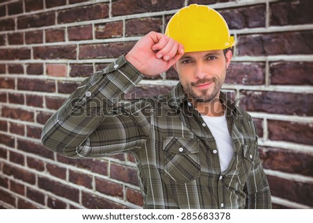 Smiling Handyman holding helmet against red brick wall