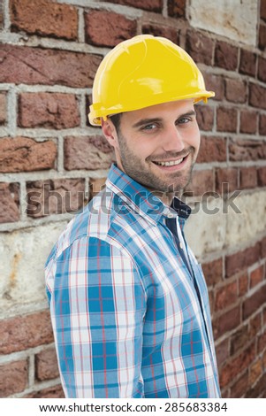 Confident repairman wearing hard hat against red brick wall