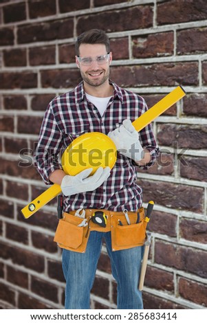 Handyman holding hard hat and spirit level against red brick wall