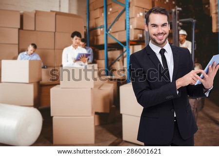 Businessman using his tablet while looking at the camera against people at work in warehouse