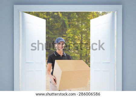 Happy delivery woman holding cardboard box against tarmac curved country road in forest