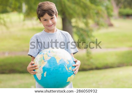 Smiling boy holding an earth globe in the park on a sunny day