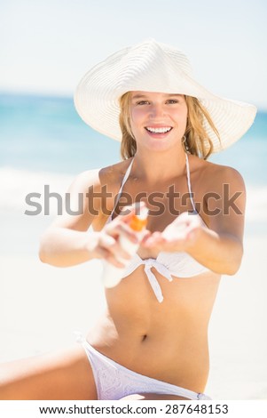 Pretty blonde woman putting sun tan lotion on her hand at the beach
