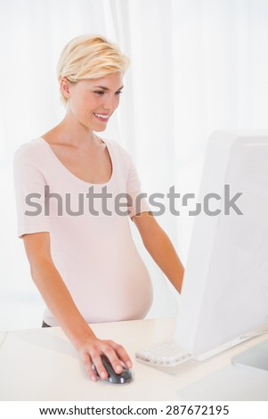 Smiling of a blonde pregant using computer in the office