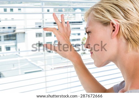Curious blonde woman looking through venetian blind on a sunny day