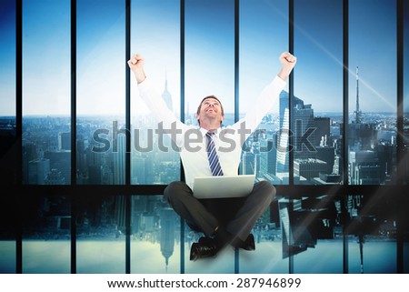 Excited cheering businessman sitting using his laptop against room with large window looking on city