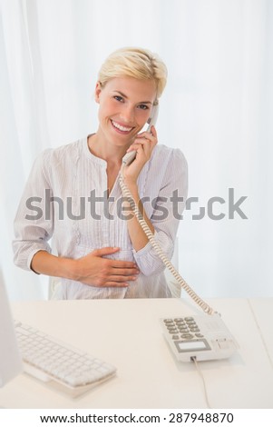 Portrait smiling blonde woman using computer and phoning in the office