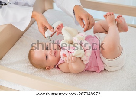 Beautiful cute baby girl with doctor taking temperature at home in bedroom