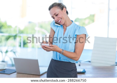 Smiling businesswoman having a phone call and taking notes in an office