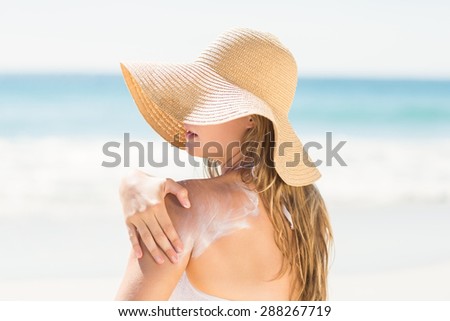 Pretty blonde woman spreading sun tan lotion on her shoulder at the beach