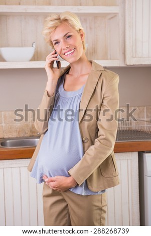 Smiling blonde pregnancy phoning in the kitchen
