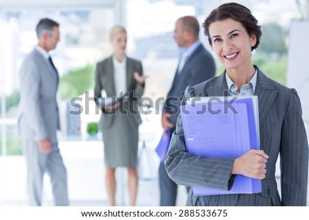 Smiling businesswoman holding files and looking at camera in the office