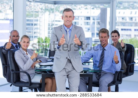Business team smiling at camera showing thumbs up in the office