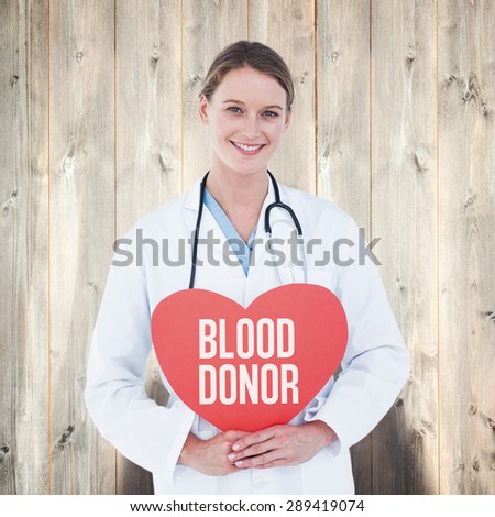 Doctor holding red heart card against pale wooden planks