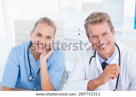 Smiling doctor and nurse looking at camera in medical office