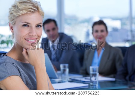 Businesswoman smiling at camera with colleagues behind in the office