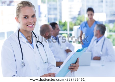 Smiling female doctor looking at camera while her colleages works in medical office