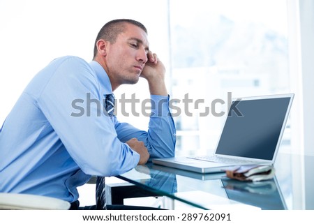 Tired businessman looking at his laptop in an office