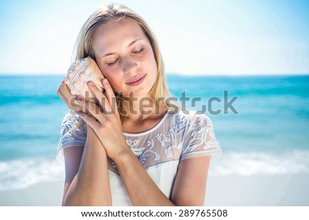 Lovely woman listening to a shell at the beach