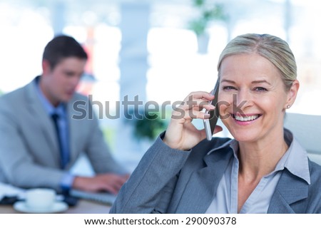 Smiling businesswoman having a phone call with colleague in background in an office